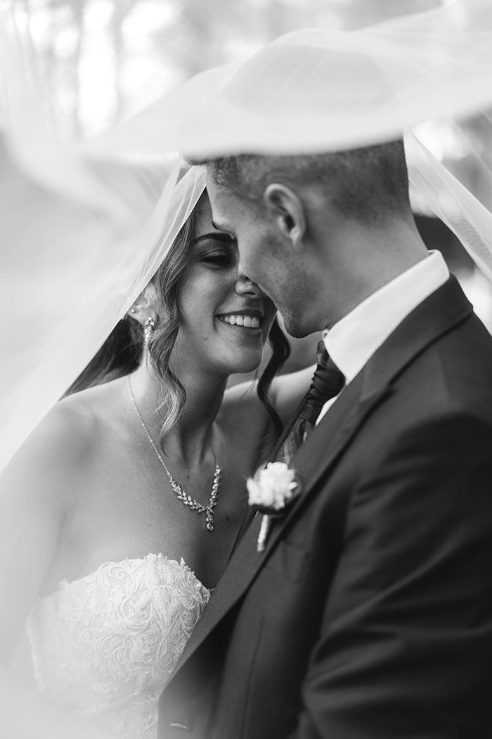 Una fotografía en blanco y negro de una novia y un novio bajo un velo.