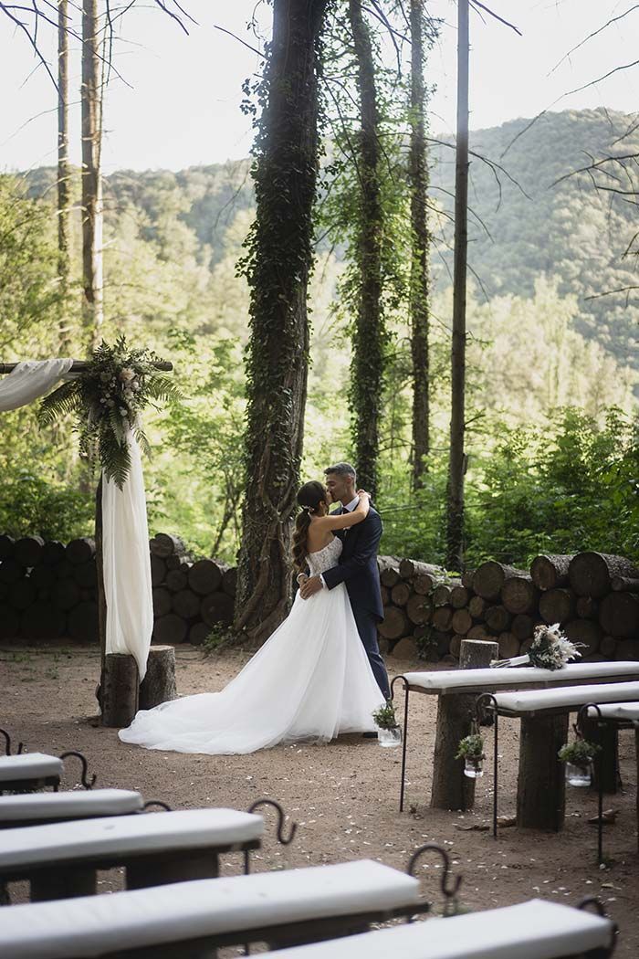 Una novia y un novio se besan en el bosque en su ceremonia de boda.