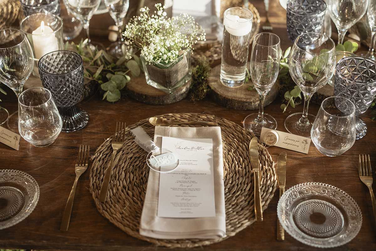 Una mesa de madera con platos, cubiertos, vasos y un menú sobre ella.