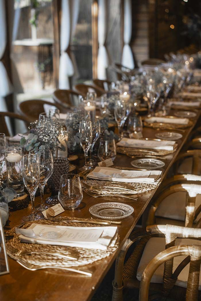 Una mesa larga de madera con platos, vasos y servilletas preparadas para una cena.