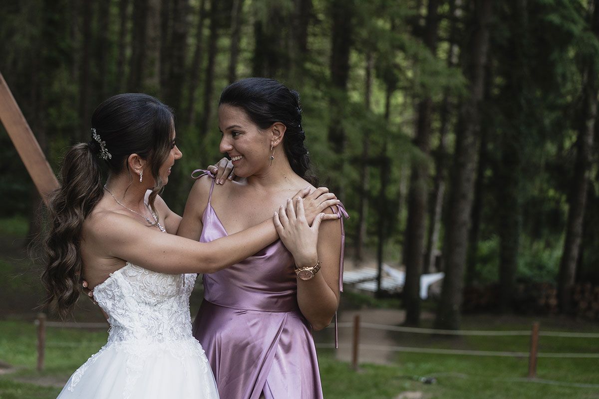 Una novia y su dama de honor posan para una fotografía en el bosque.