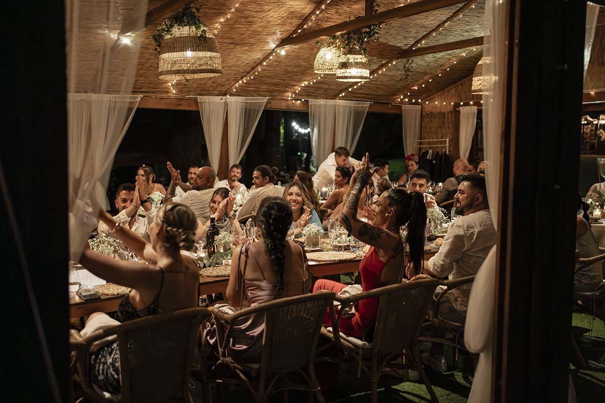 Un grupo grande de personas están sentadas en mesas en una recepción de boda.