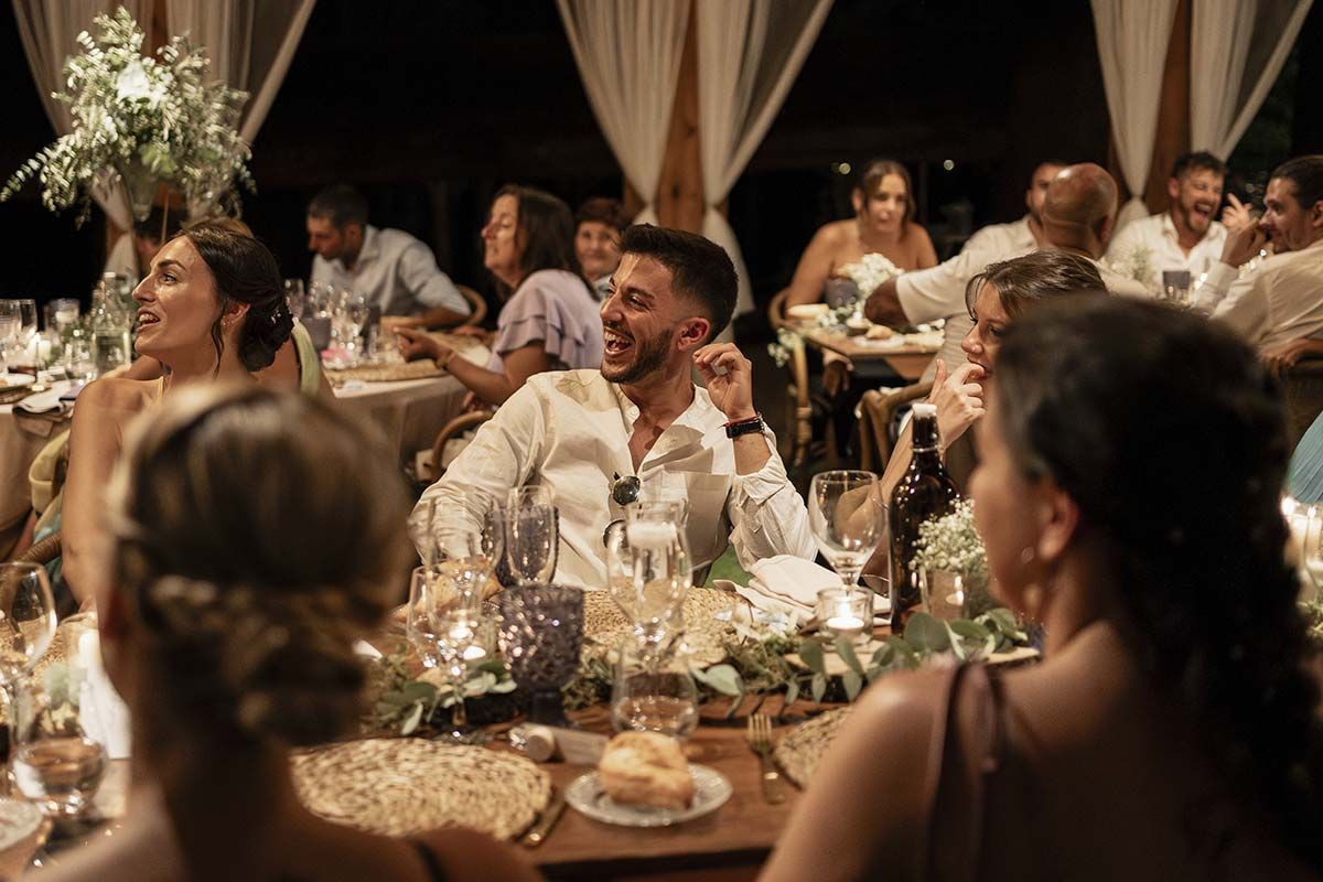 Un grupo de personas están sentadas en mesas en una recepción de boda.