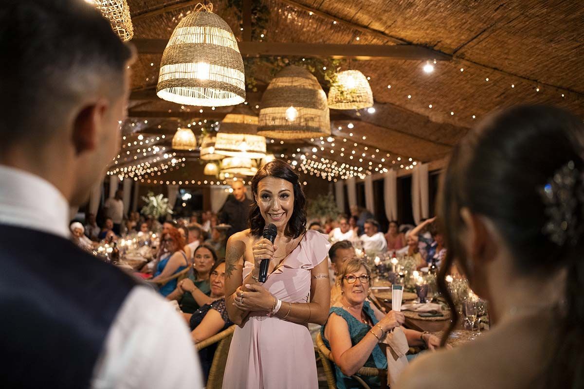 Una mujer sostiene un micrófono frente a un hombre en una recepción de boda.