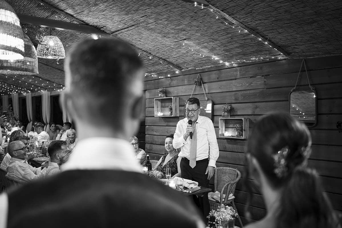 Un hombre está dando un discurso en una recepción de boda en una fotografía en blanco y negro.