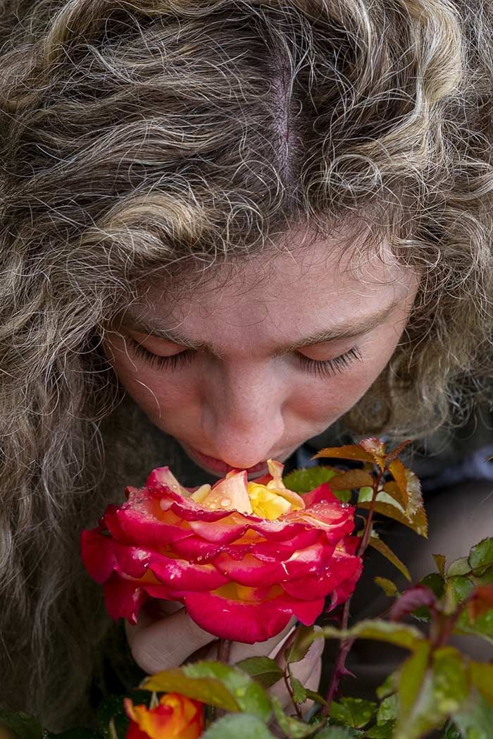 Una mujer huele una rosa roja con los ojos cerrados.
