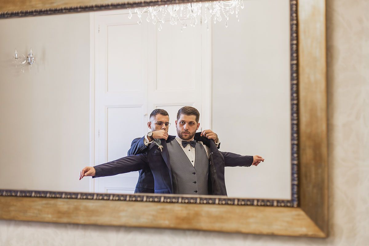 Dos hombres se preparan para una boda frente a un espejo.