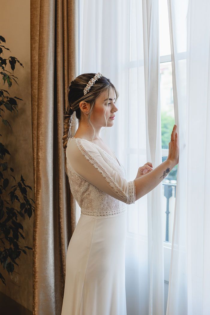 Una mujer con un vestido de novia está parada frente a una ventana.