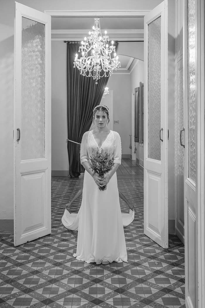 Una novia con un vestido de novia está parada en un pasillo sosteniendo un ramo de flores.