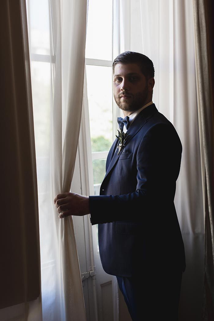 Un hombre con traje está parado frente a una ventana.