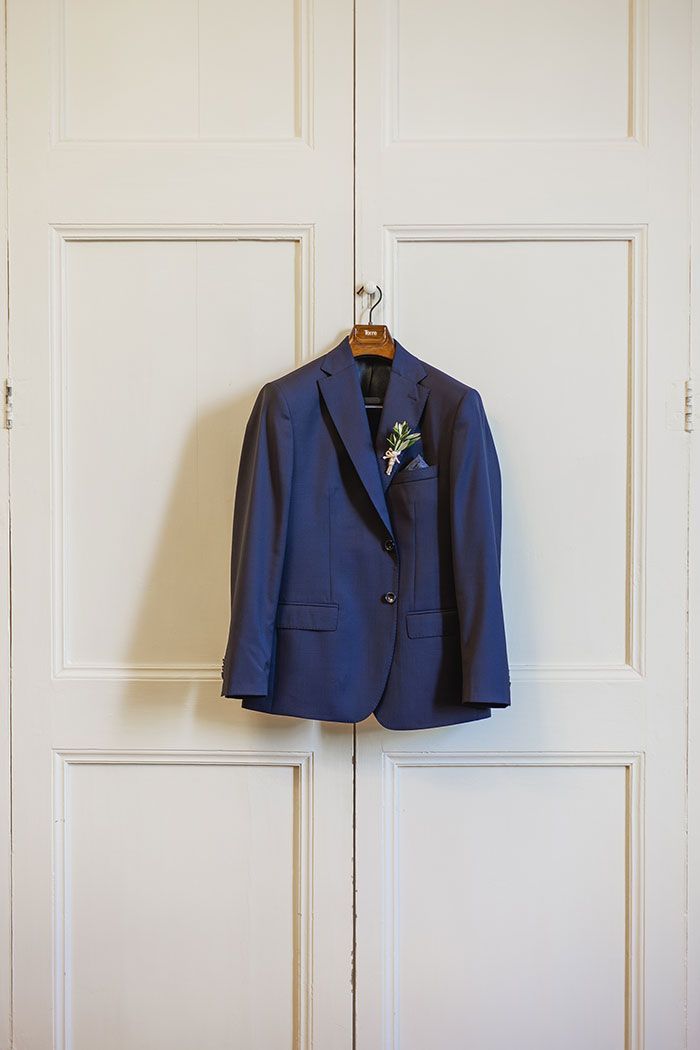 Una chaqueta de traje azul cuelga de una percha de madera en una puerta blanca.