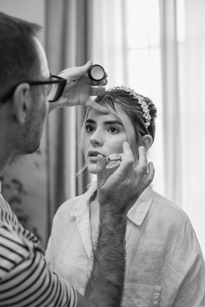 Un hombre está aplicando maquillaje en el rostro de una mujer en una fotografía en blanco y negro.