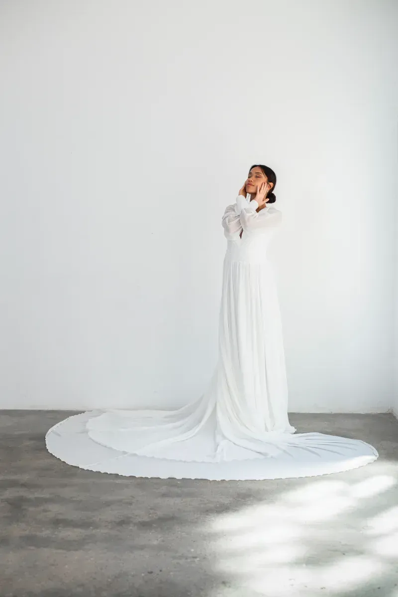 Una mujer con un vestido largo blanco está parada en una habitación.