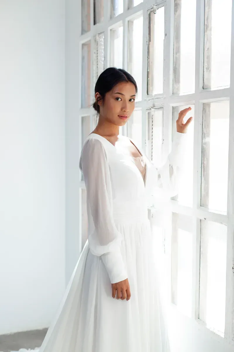 Una mujer con un vestido blanco está parada frente a una ventana.