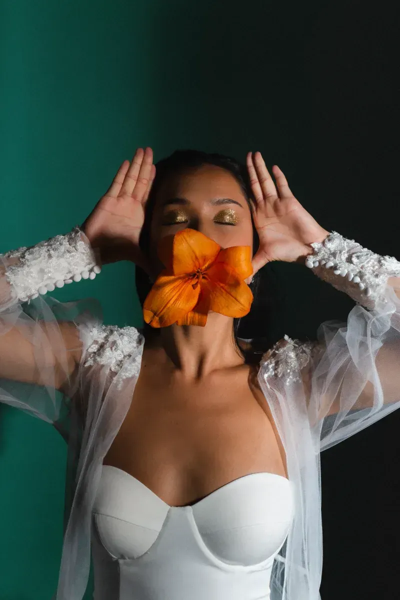 Una mujer con un vestido blanco sostiene una flor en la boca.