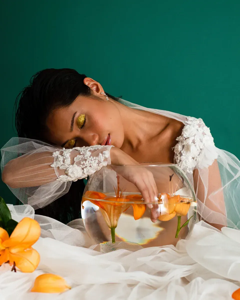 Una mujer con un vestido blanco está acostada junto a una pecera llena de flores.