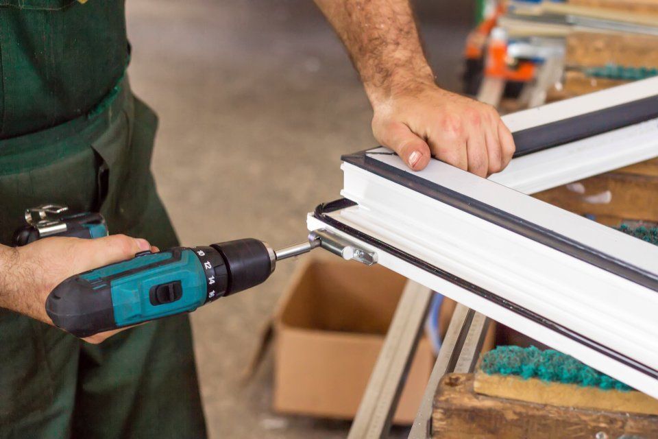 Ein Mann repariert mit einer Bohrmaschine einen Fensterrahmen.