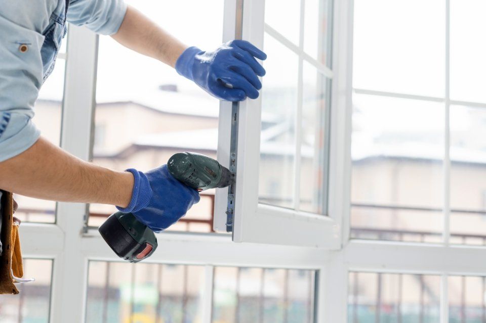 Ein Mann baut mit einer Bohrmaschine ein Fenster ein.