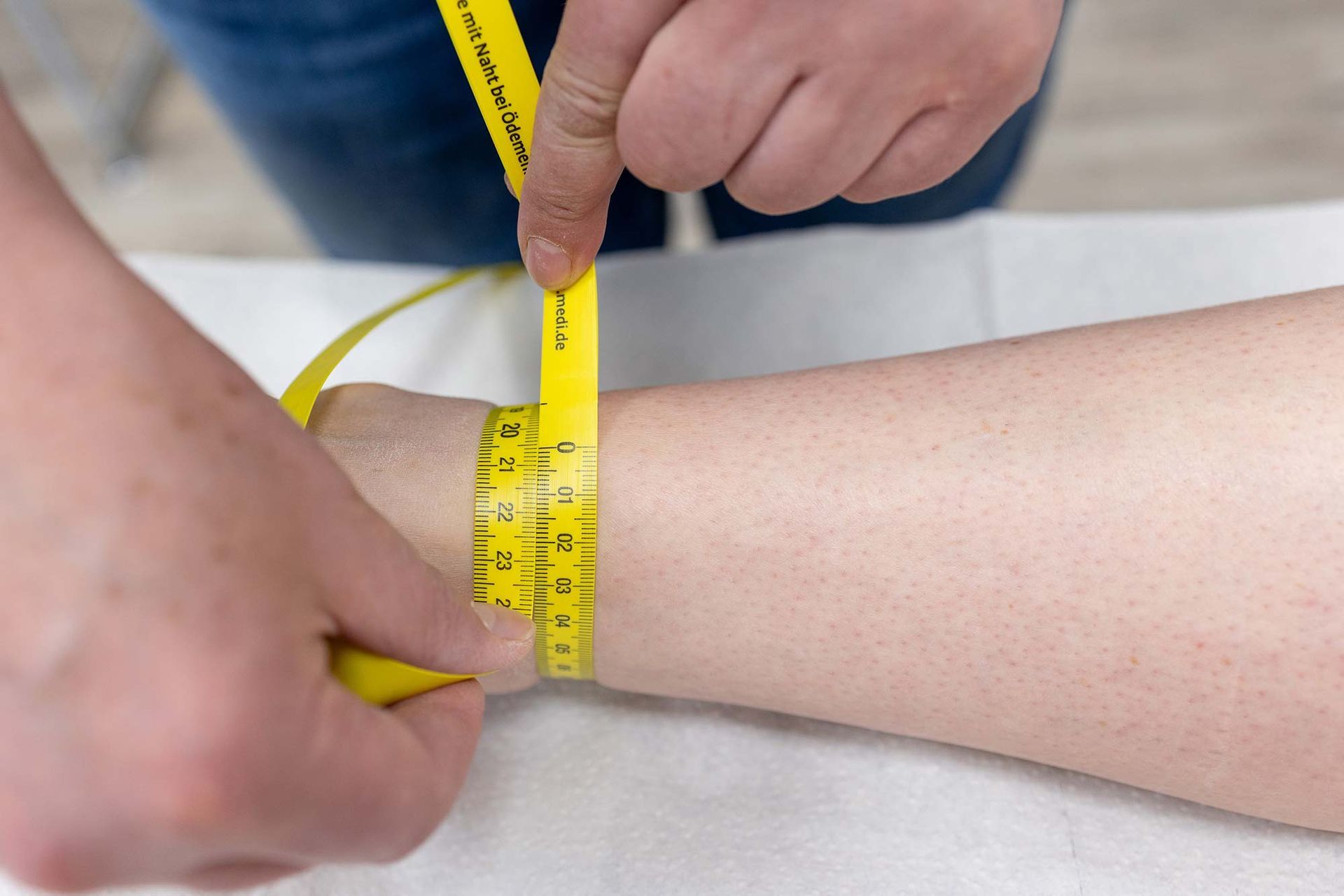 Eine Person misst das Handgelenk einer anderen Person mit einem gelben Maßband.