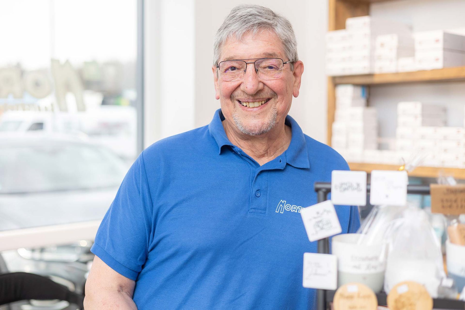 Ein Mann mit Brille und blauem Hemd lächelt in einem Geschäft.