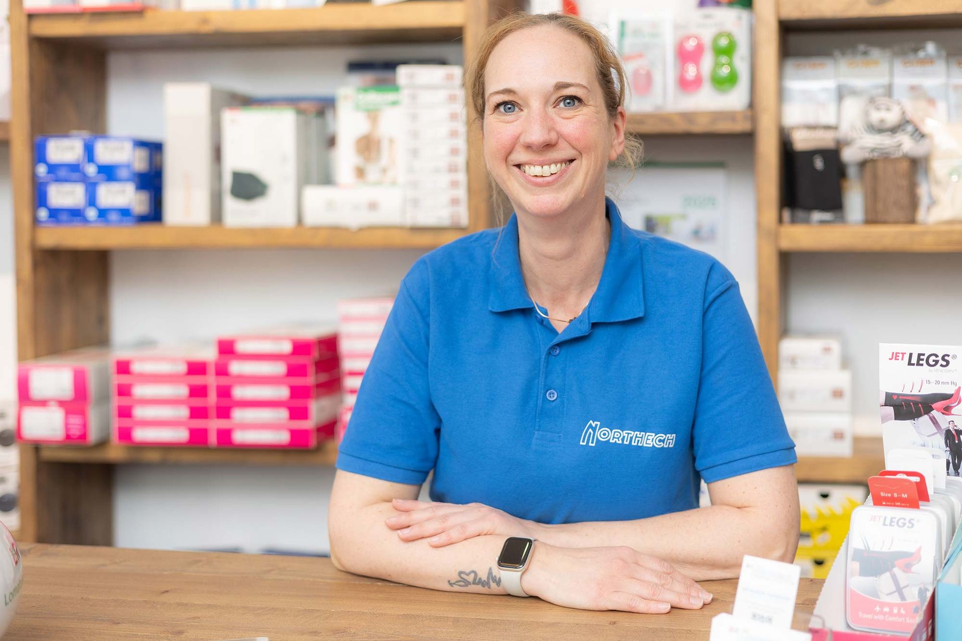 Eine Frau in einem blauen Hemd sitzt an einem Tresen in einer Apotheke.