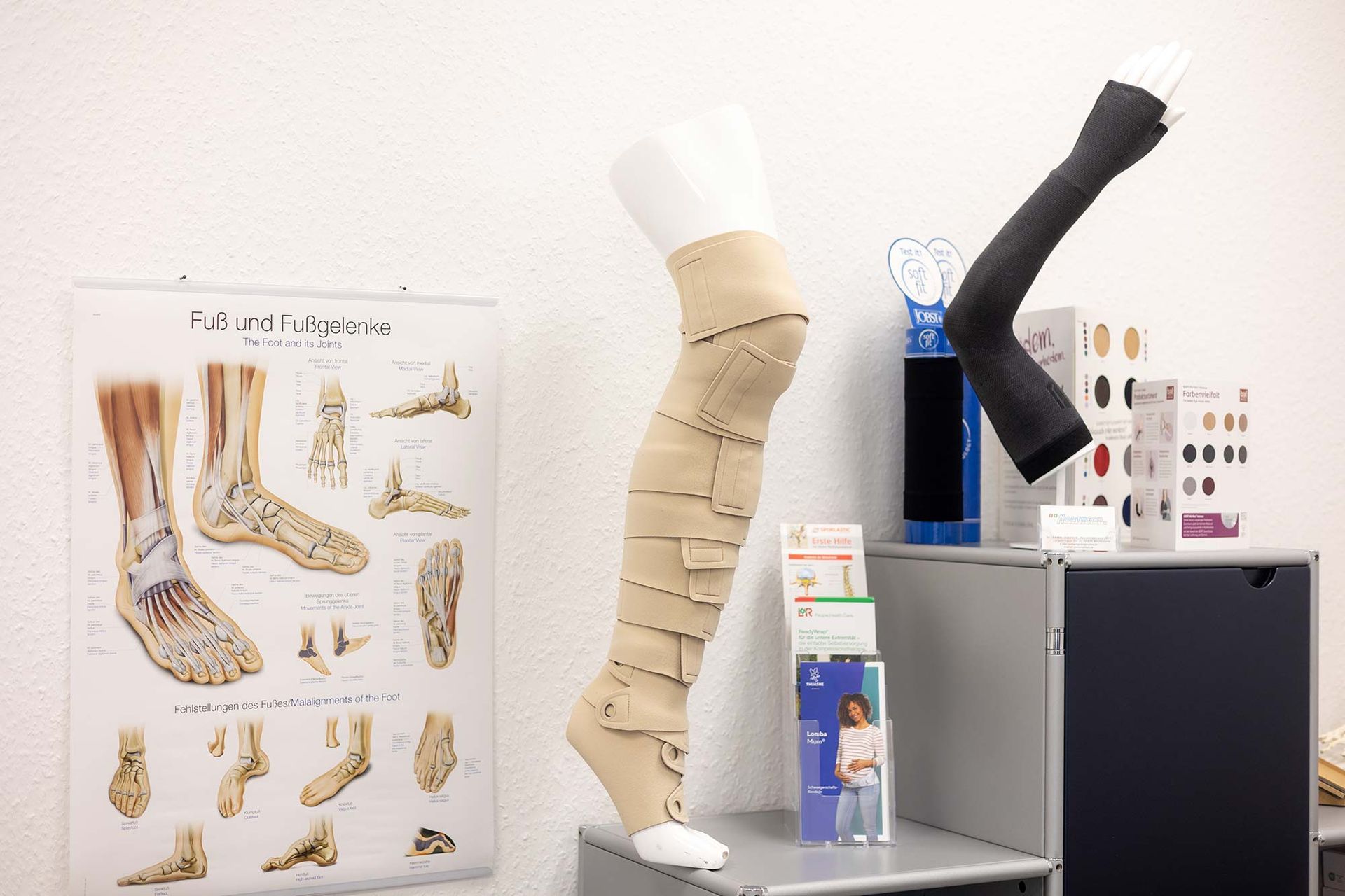 Eine Schaufensterpuppe mit einem Verband am Bein sitzt auf einem Tisch in einem Raum.