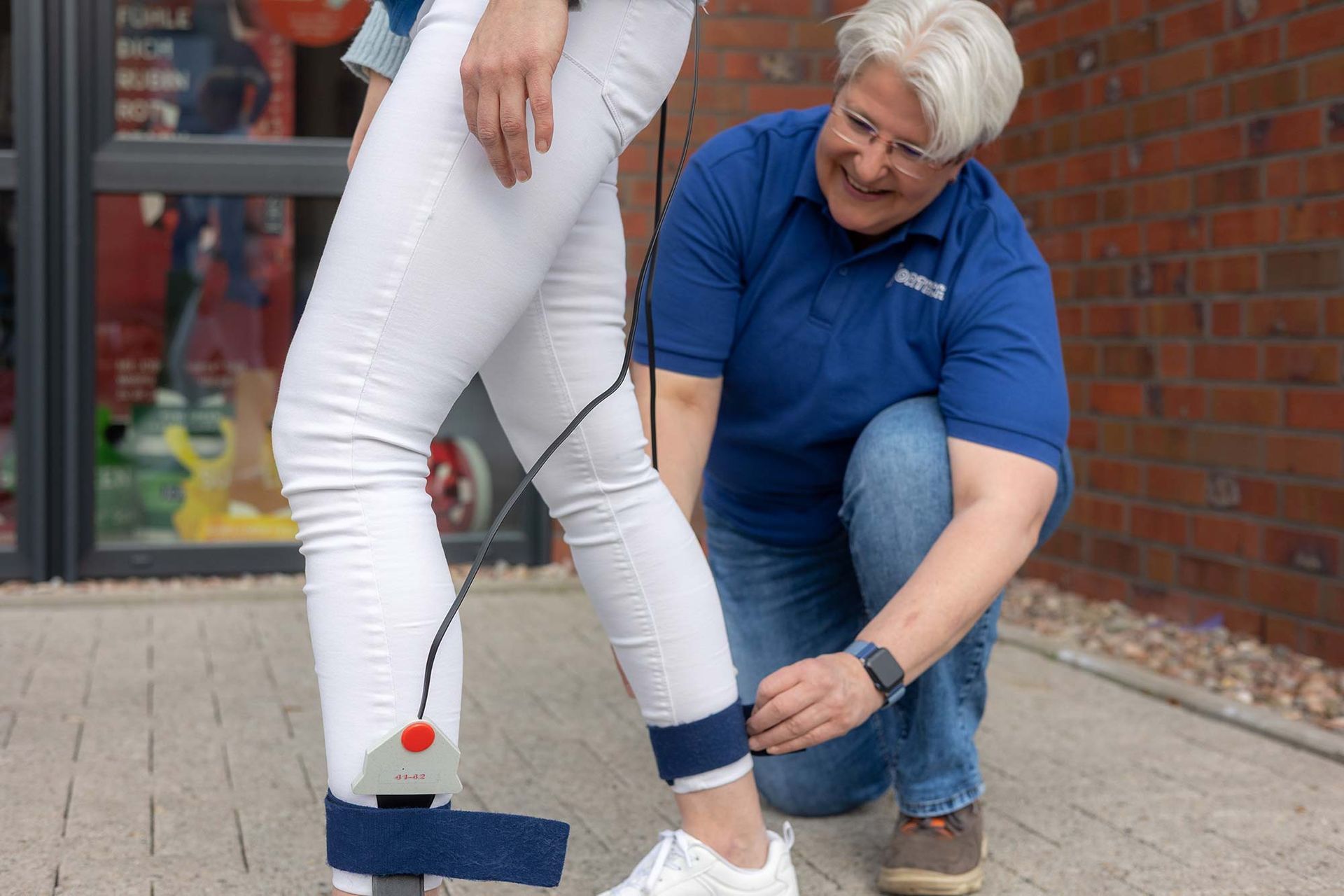 Eine Frau kniet neben dem Bein einer anderen Frau mit einem Verband.