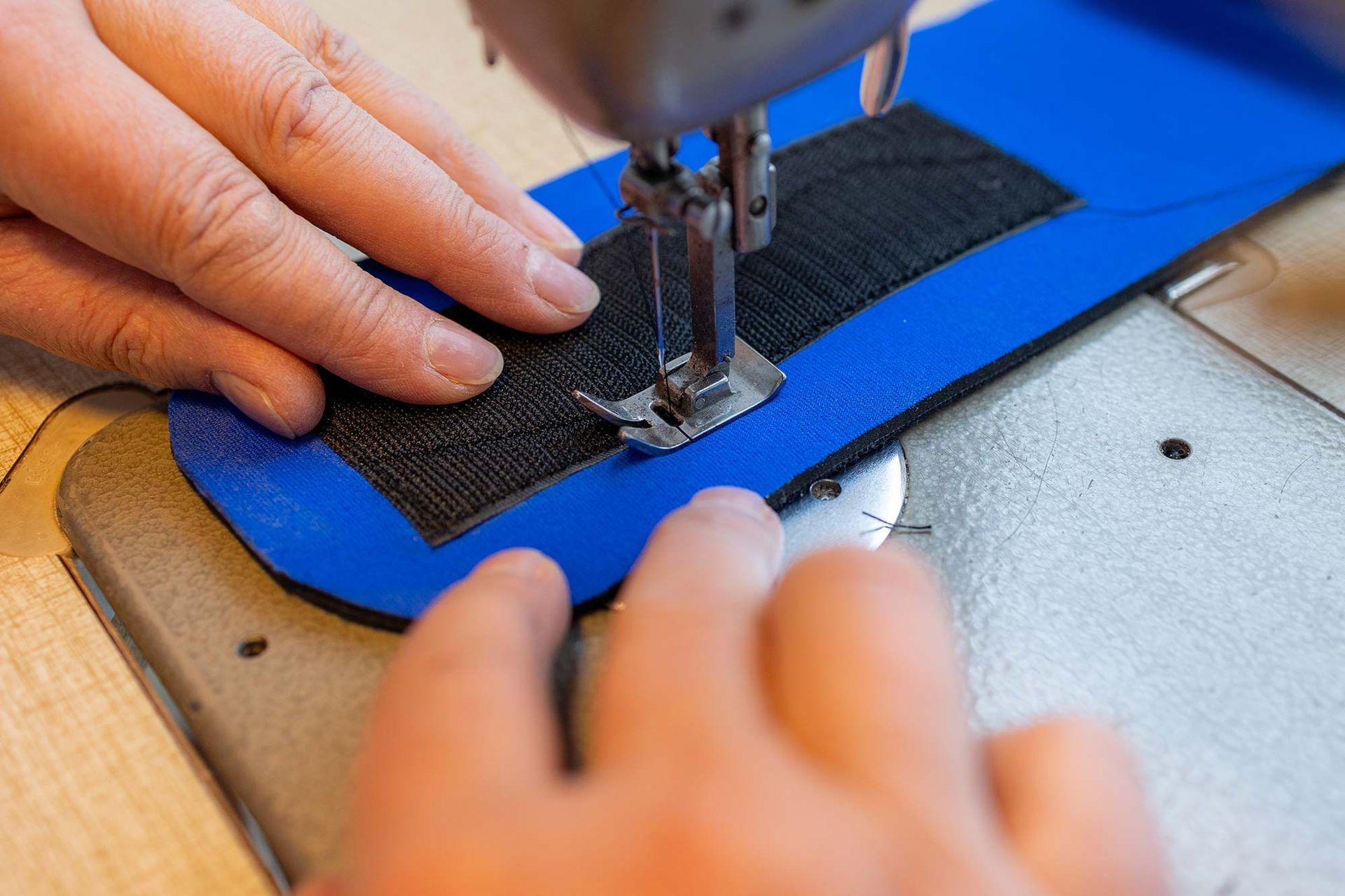 Eine Person näht mit einer Nähmaschine ein Stück blauen Stoff.