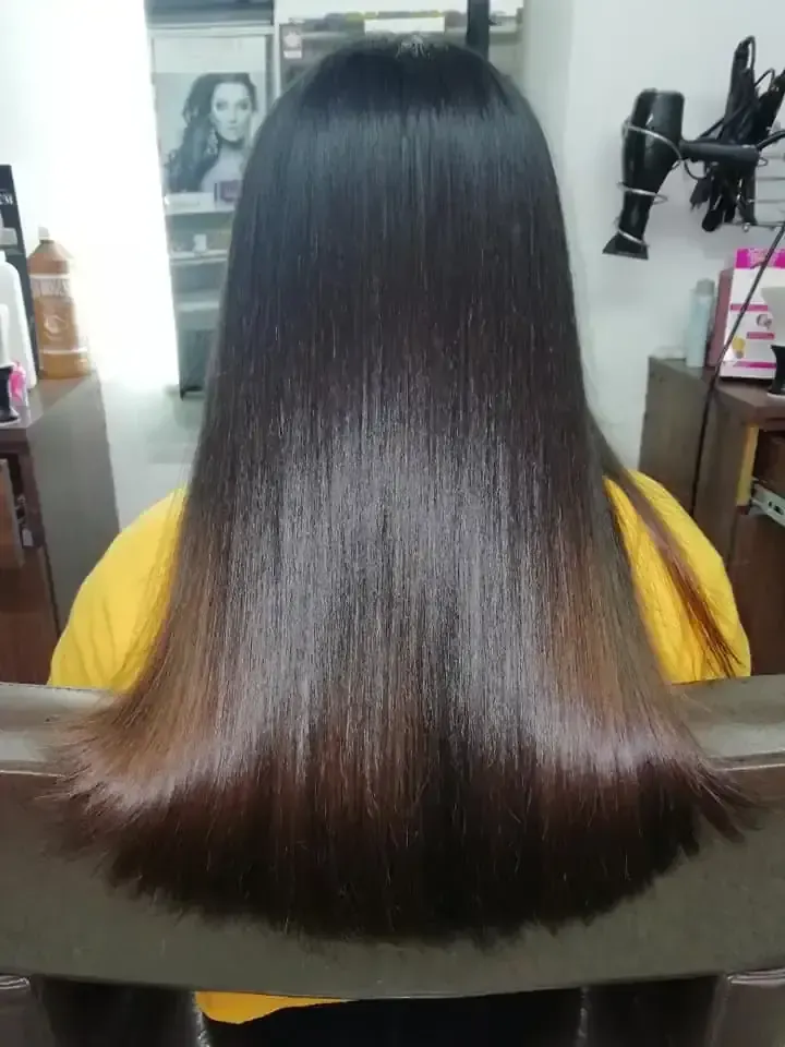 Cabello largo, liso y oscuro con efecto ombré, peinado en un salón, persona vestida con una camisa amarilla.