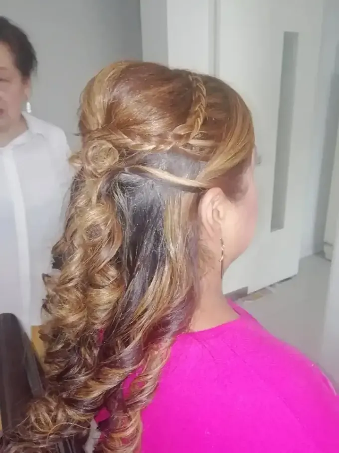Mujer con cabello castaño rizado y peinado, con trenza parcial y un top rosa.