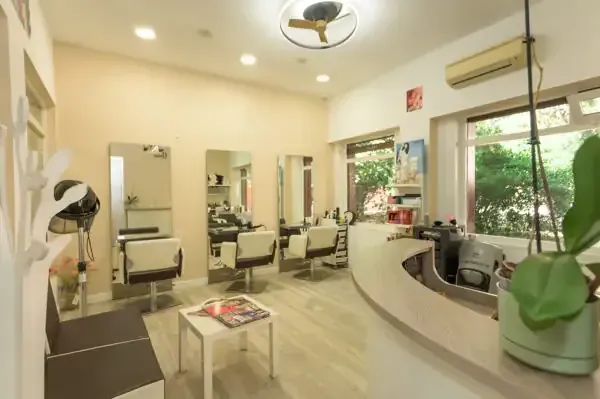 Interior de peluquería con espejos, estaciones de peinado y mostrador de recepción.