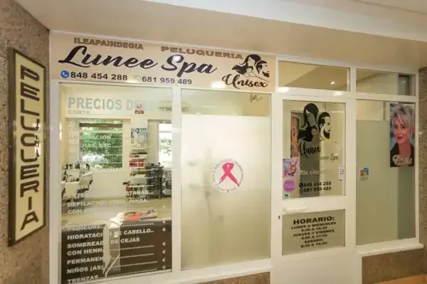 Exterior del salón "Lunee Spa" con escaparate y señalización; cinta rosa de concientización sobre el cáncer de mama visible.