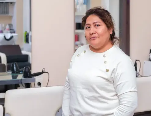 Una mujer con un suéter blanco está parada en una peluquería, mirando a la cámara.