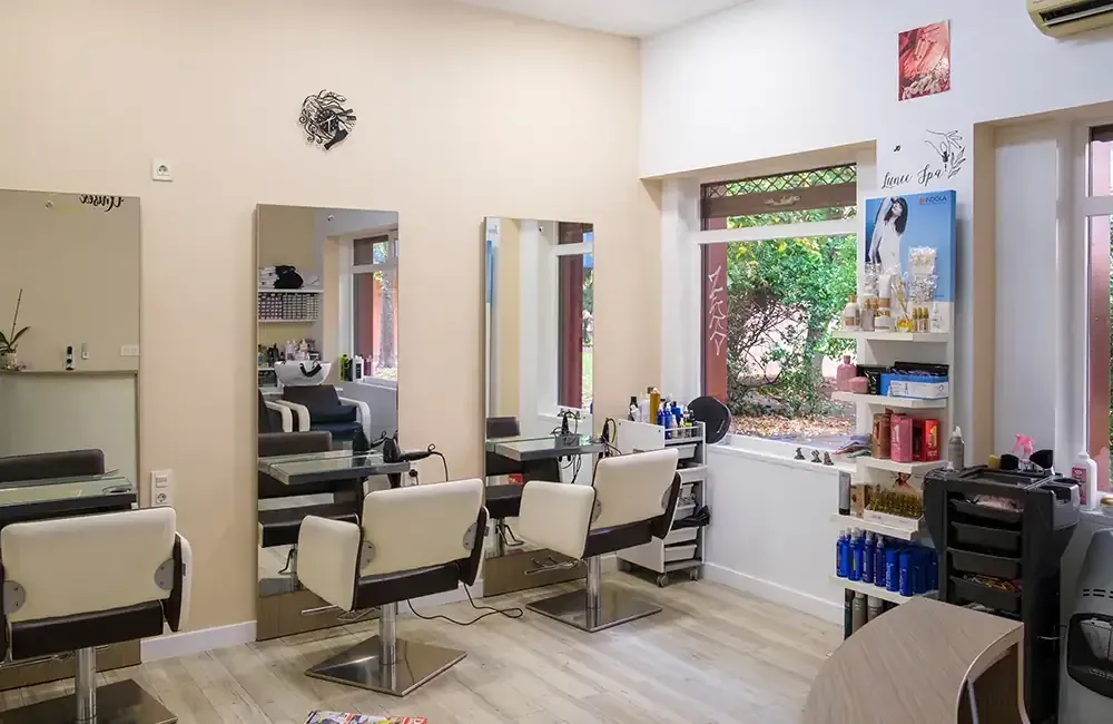 Una mujer con cabello oscuro sonríe, usando maquillaje, en una peluquería.
