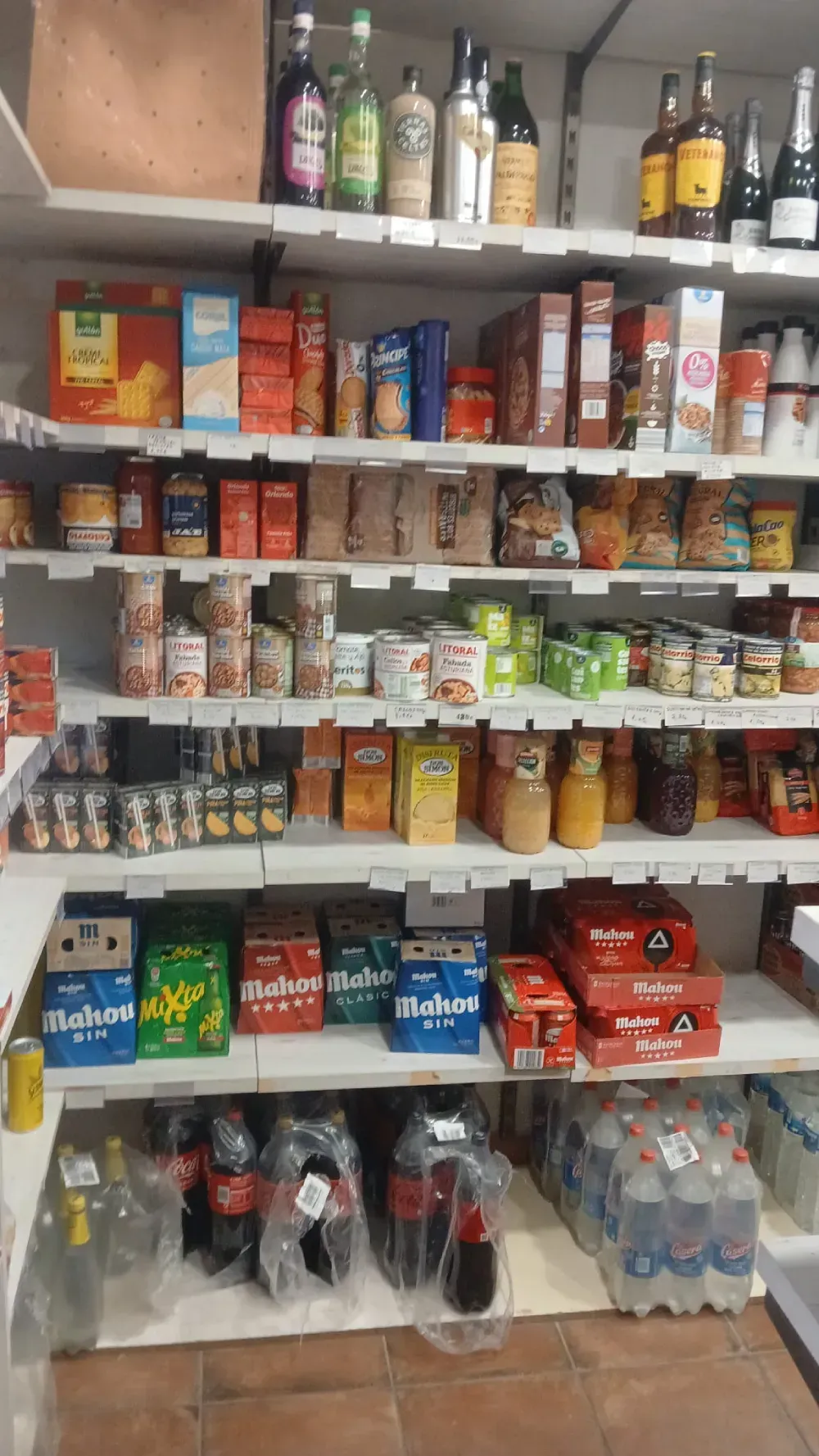 Estantes repletos de comestibles, incluidos alimentos enlatados, cereales y bebidas, en un entorno de tienda.