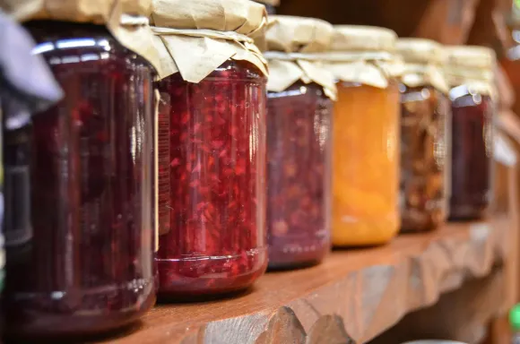 Tarros de conservas de colores sobre un estante de madera, varios tonos de rojo y naranja, tapas de papel marrón.
