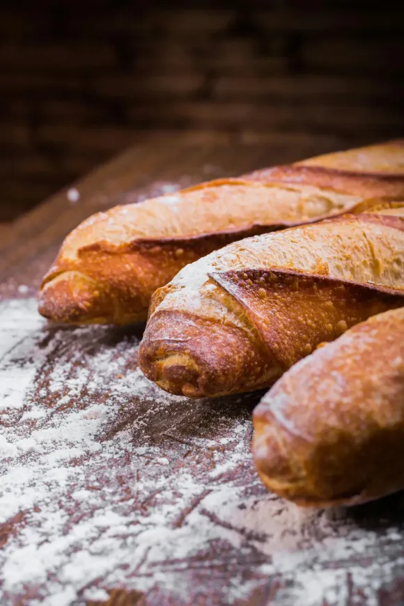 Tres baguettes espolvoreadas con harina sobre una superficie de madera.