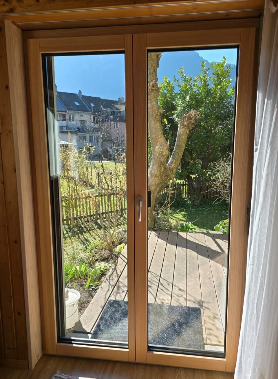 Doppeltüren mit Holzrahmen und Blick auf einen sonnigen Hinterhof und entfernte Gebäude.