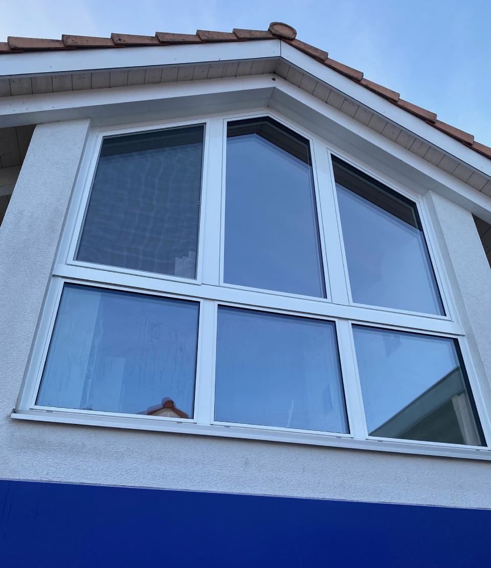 Weiss gerahmte Fenster mit einem dreieckigen oberen Abschnitt an einem Gebäude, in dem sich der Himmel spiegelt.