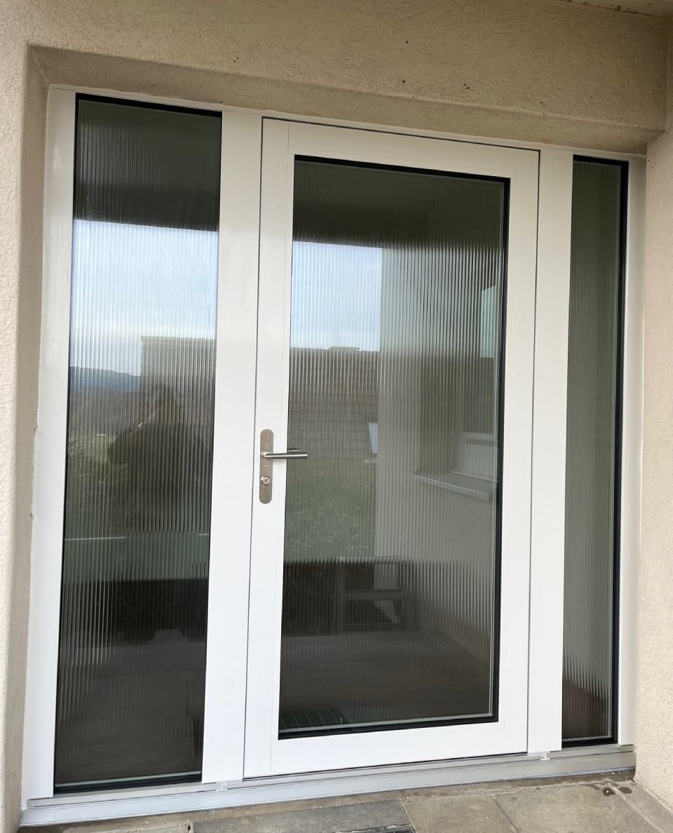 Weisse Doppeltüren mit strukturiertem Glas und Seitenlicht an einem hellen Gebäude.