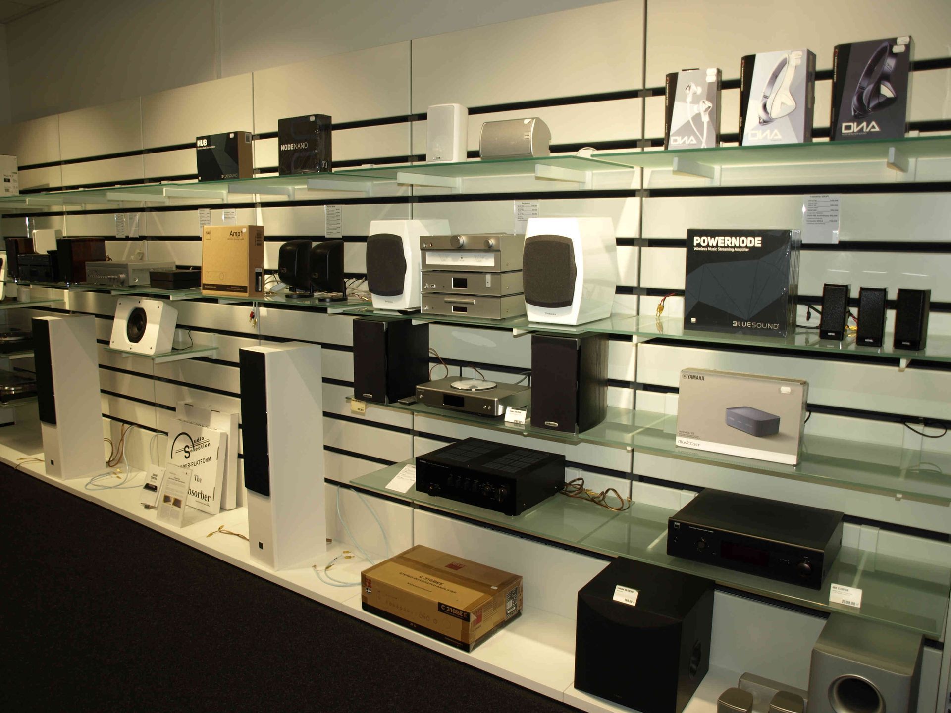 Regale mit elektronischen Geräten in einem Geschäft. Zu den Produkten gehören Lautsprecher und Smart-Home-Geräte.