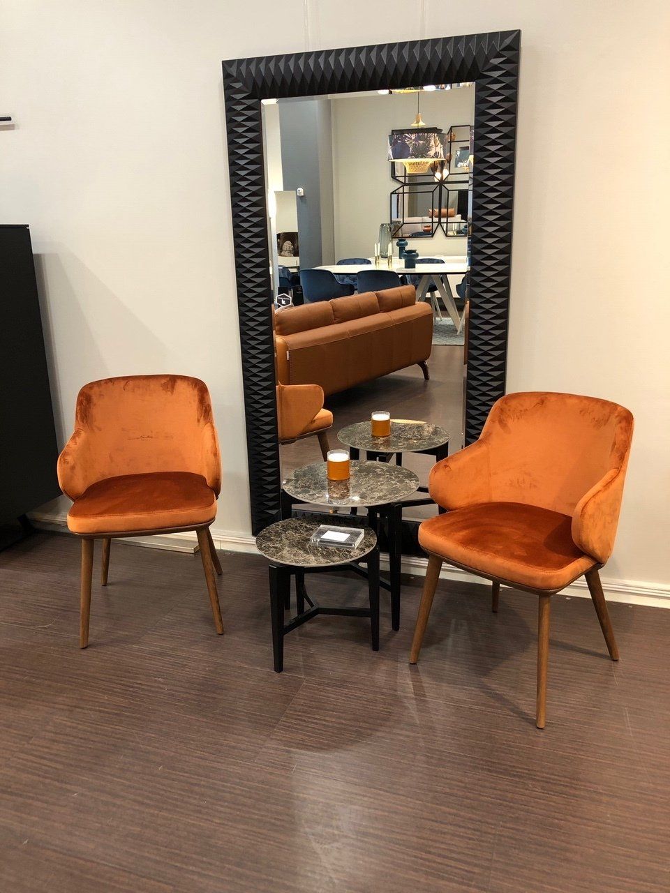 Entrée aménagée avec deux chaises en velours orange, un grand miroir et une table basse effet marbre