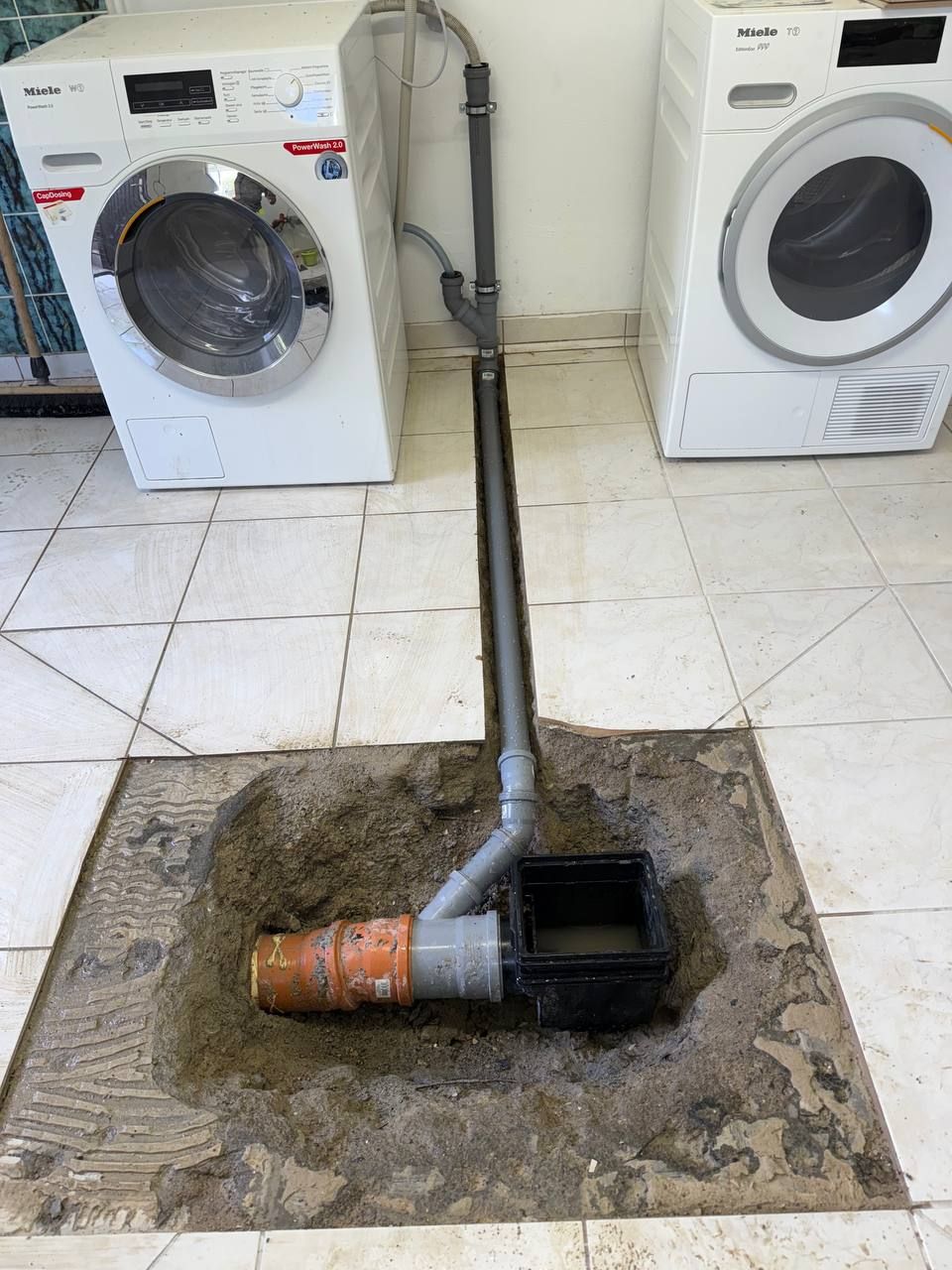Zwei Regenwasserablaufgitter neben einem Bordstein entlang einer gepflasterten Straße, links davon Gras.