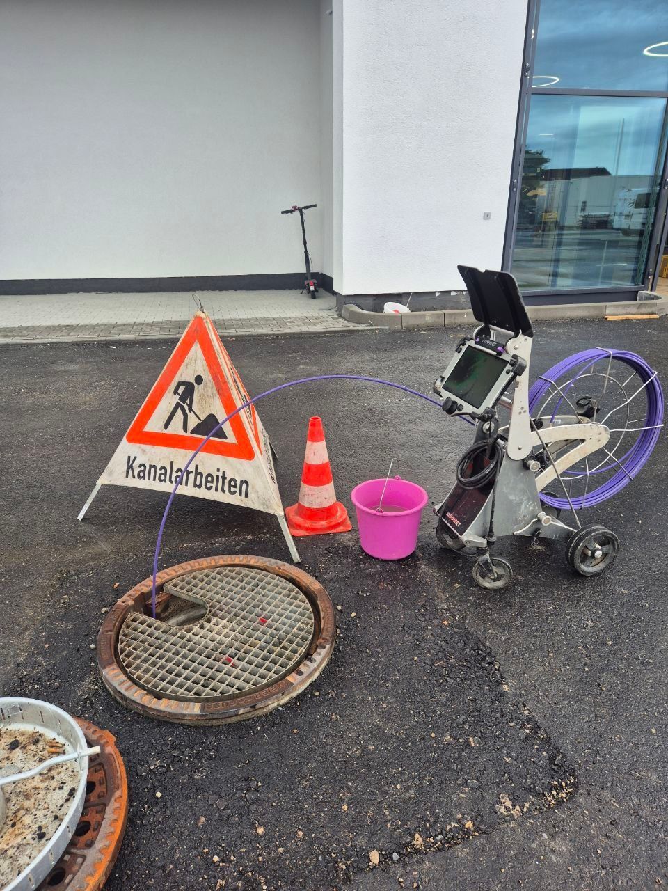Schwarzes, kamera-/drohnenähnliches Gerät wurde in einen offenen Kanaldeckel auf einer Betonstraße hinabgelassen.