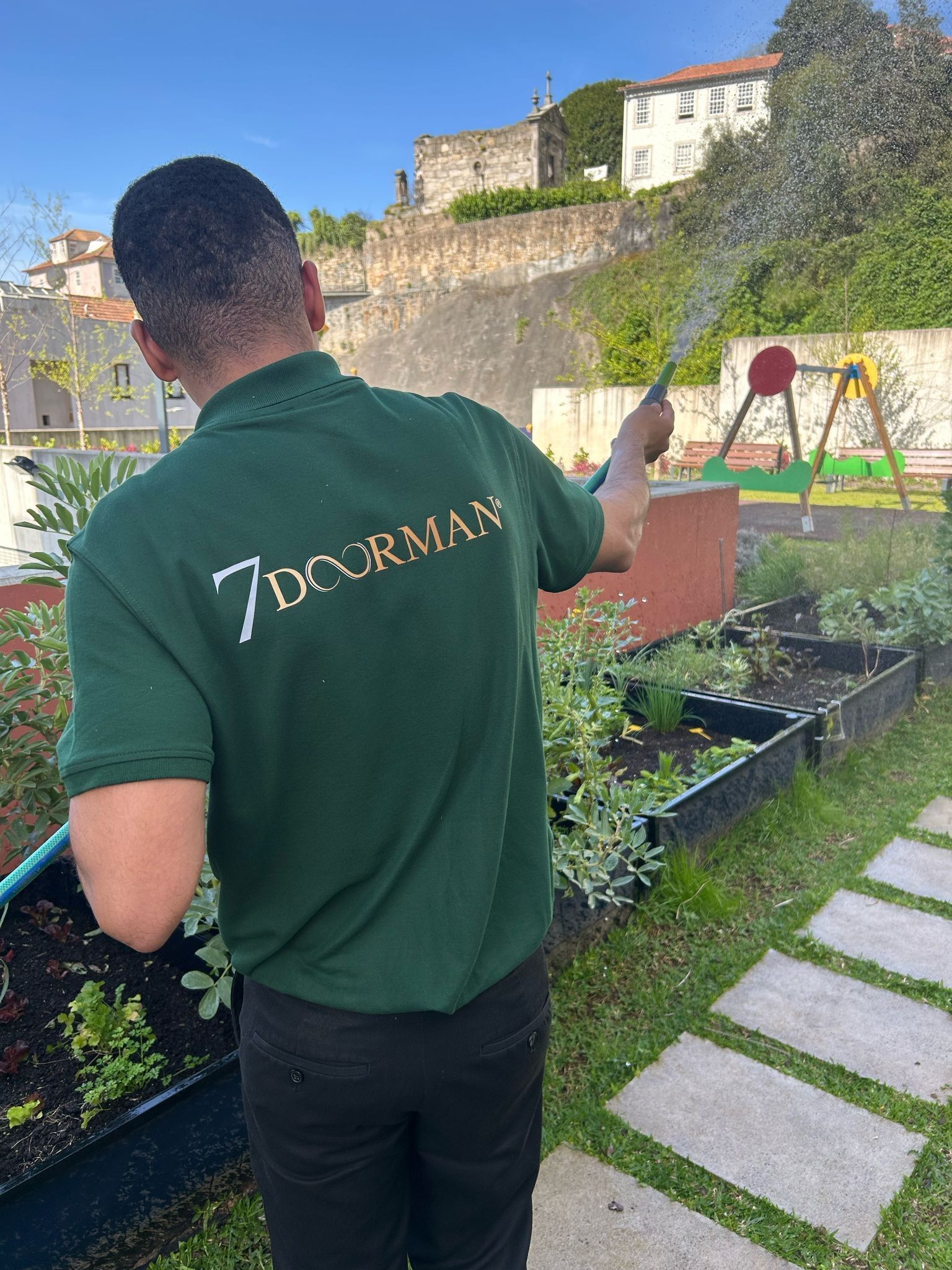 Um homem de camisa verde está regando plantas com uma mangueira.