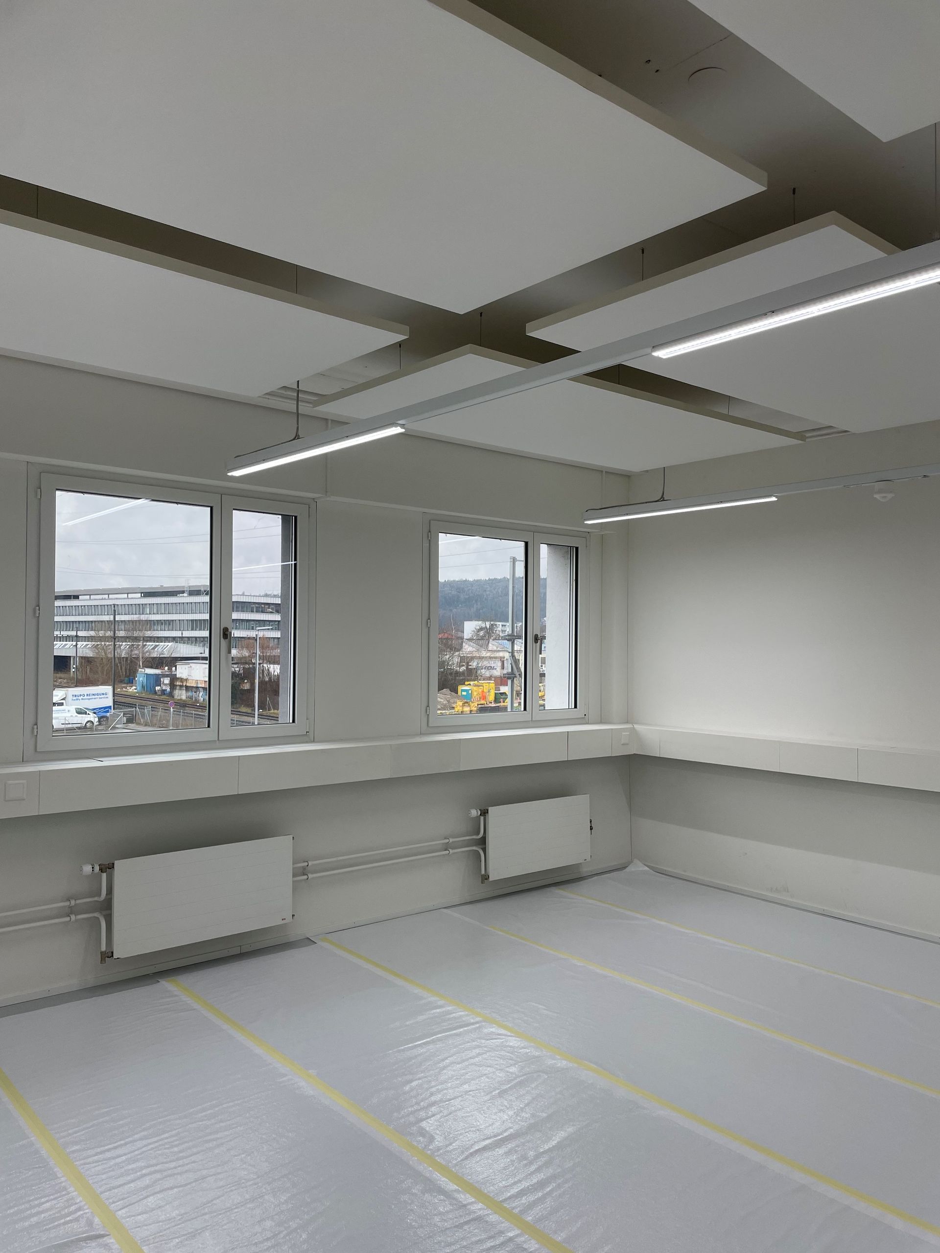 Ein Maler in blauem Overall kniet und rollt weisse Farbe auf eine Wand.