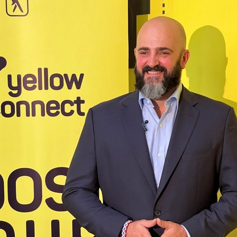 Um homem de terno está em frente a uma placa amarela que diz conexão amarela