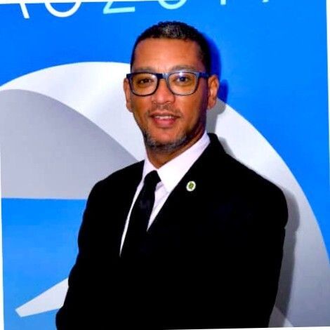 Um homem usando óculos e terno está parado em frente a um fundo azul.