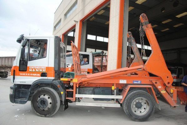 Un camión volquete naranja está estacionado frente a un edificio.
