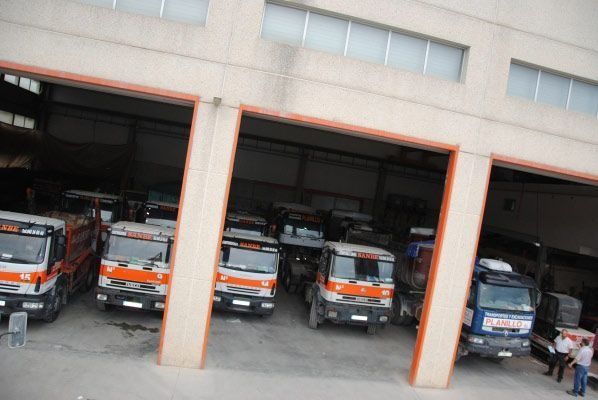 Una fila de camiones están estacionados en un garaje con un edificio al fondo.